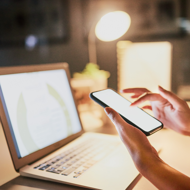 Hands using a phone and laptop to schedule posts in a social planner tool.