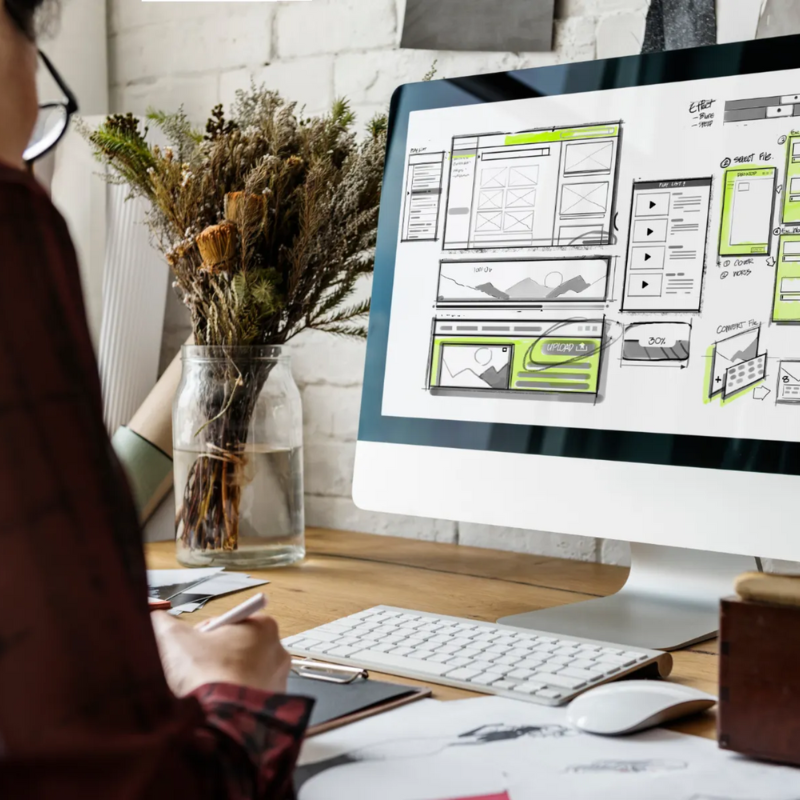 Web designer planning CTAs and fast-loading website layouts on a desktop screen with wireframe sketches and interface elements.