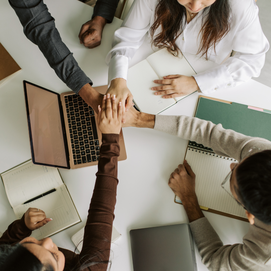 A collaborative team putting their hands in a circle by a computer while working on the elite infrastructure about MBM360.